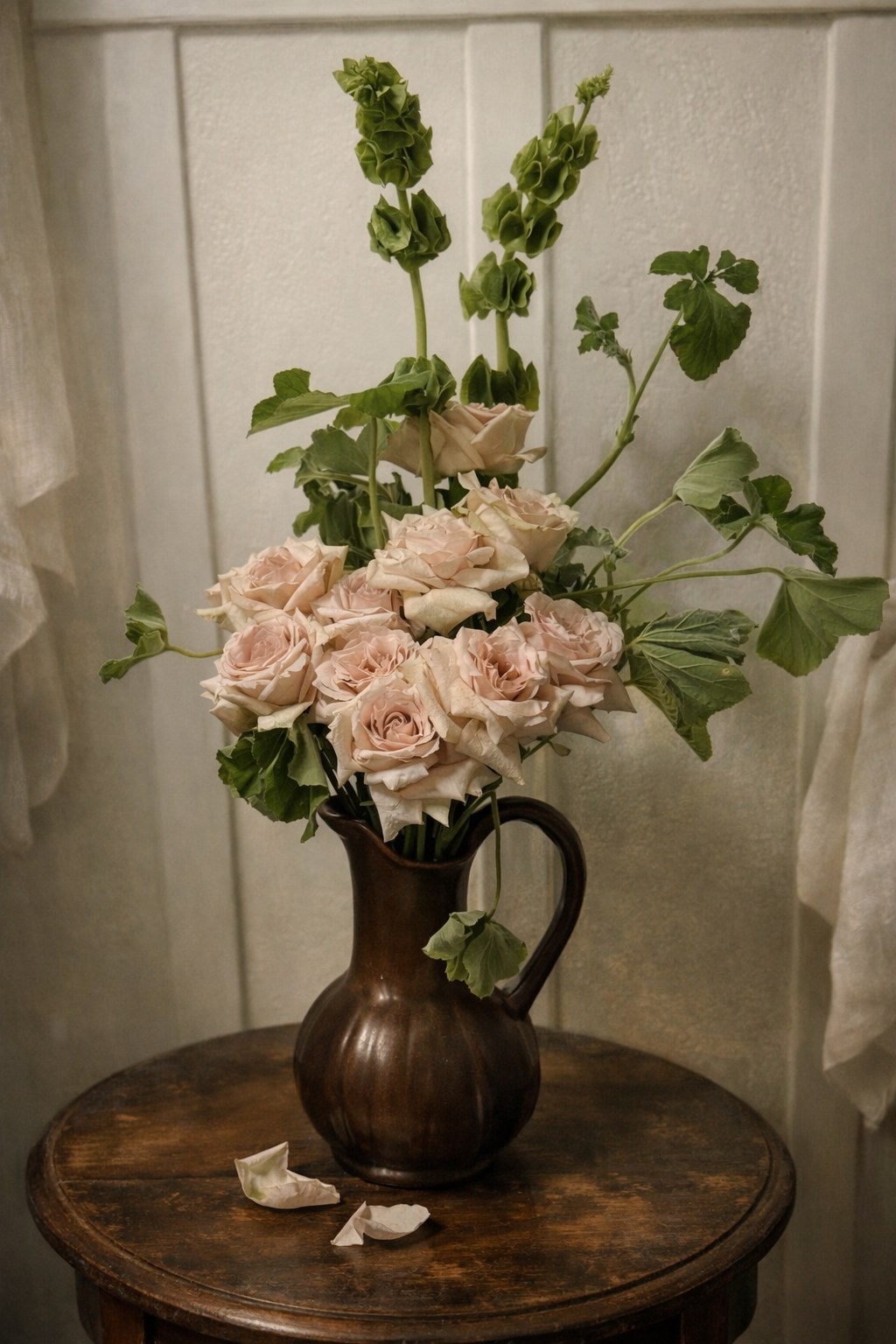 Pale rose arrangement with bells of ireland in dark ceramic pitcher