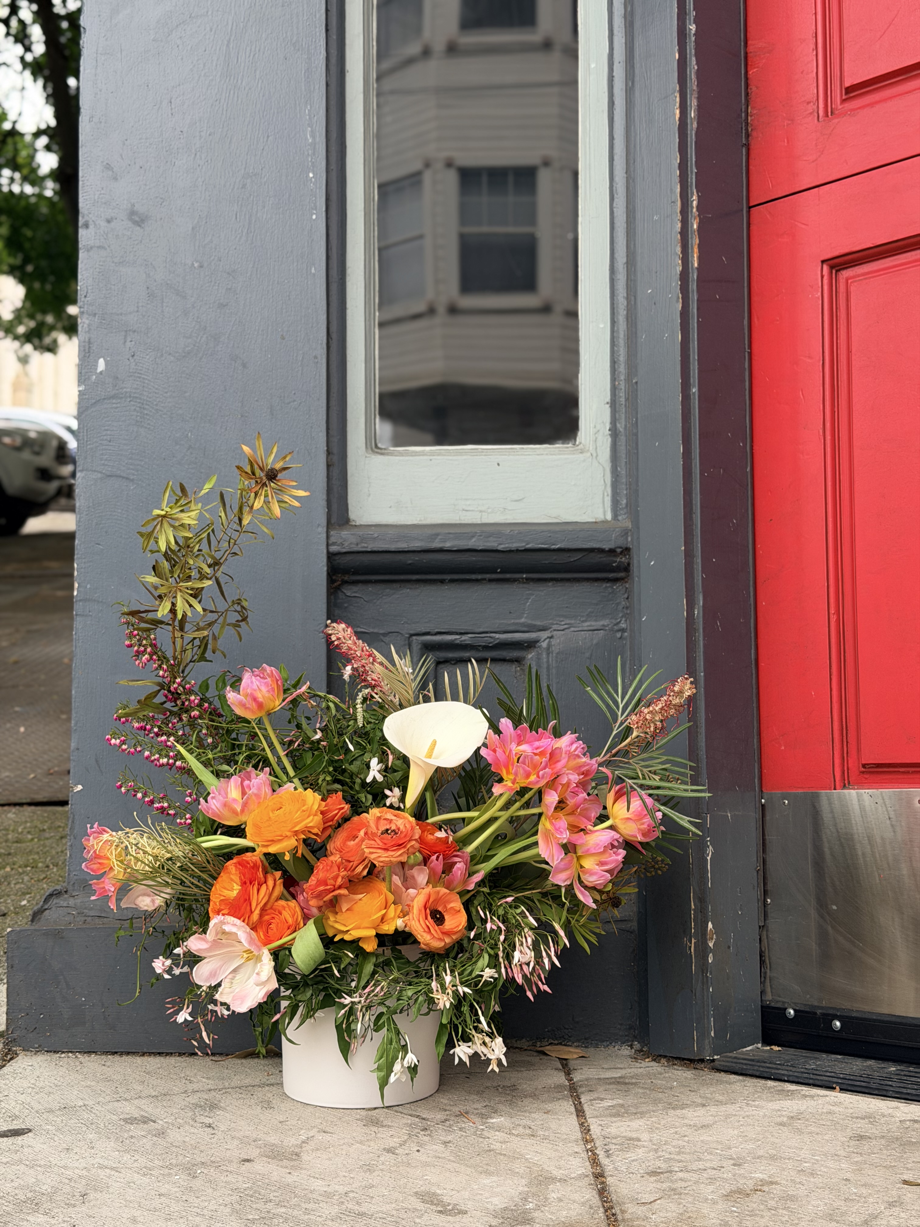 Spring arrangement by Lovely Coven with calla lily, orange ranunculus, and pink tulips against a Nob Hill doorway