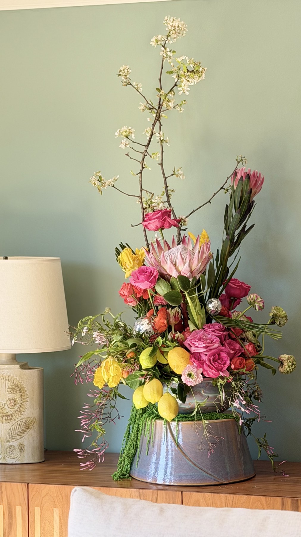 The Full Moon Summoning arrangement on credenza with lamp — king protea and lemons in iridescent vessel