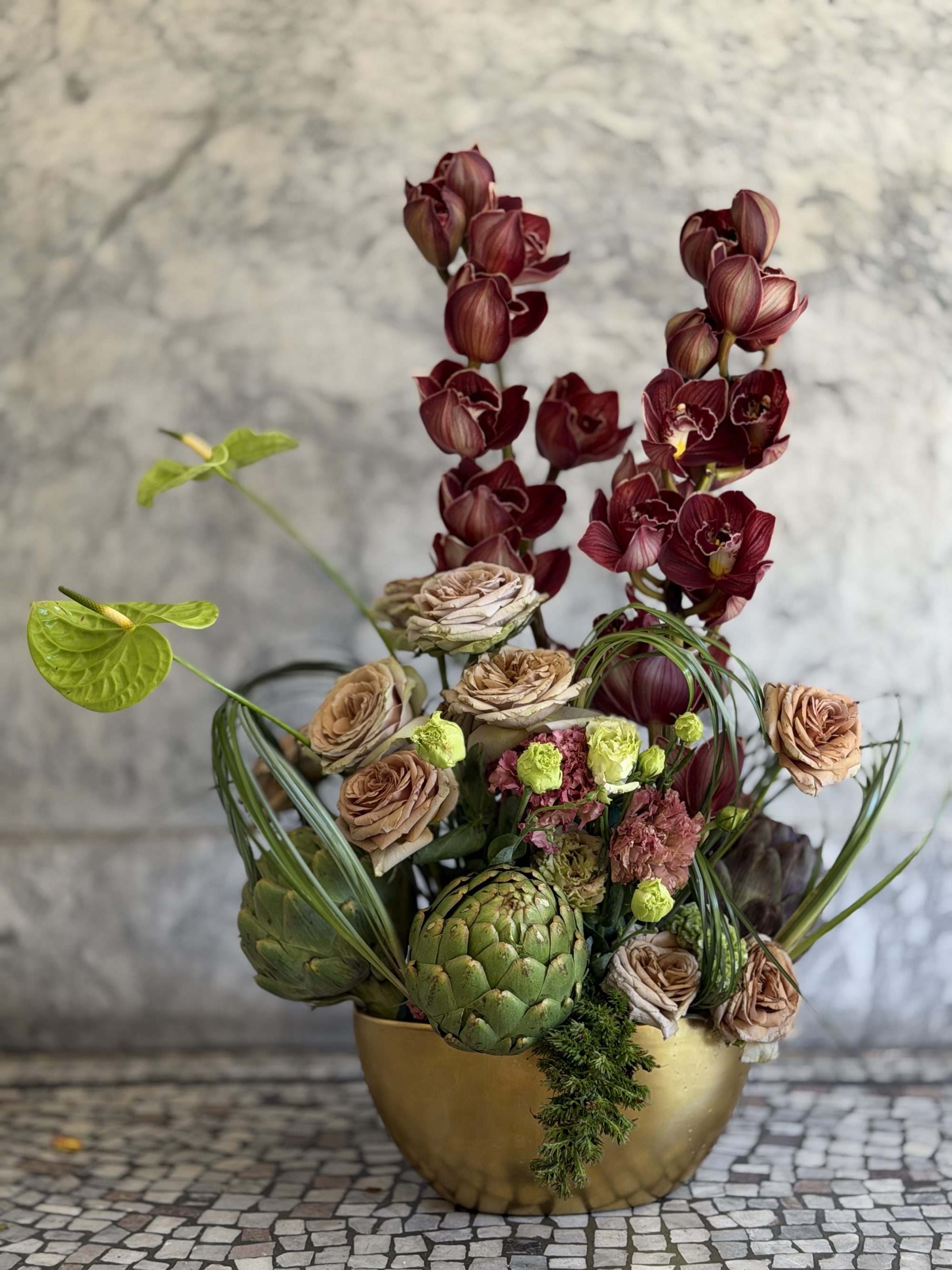 Burgundy orchids with artichokes in sculptural arrangement on marble