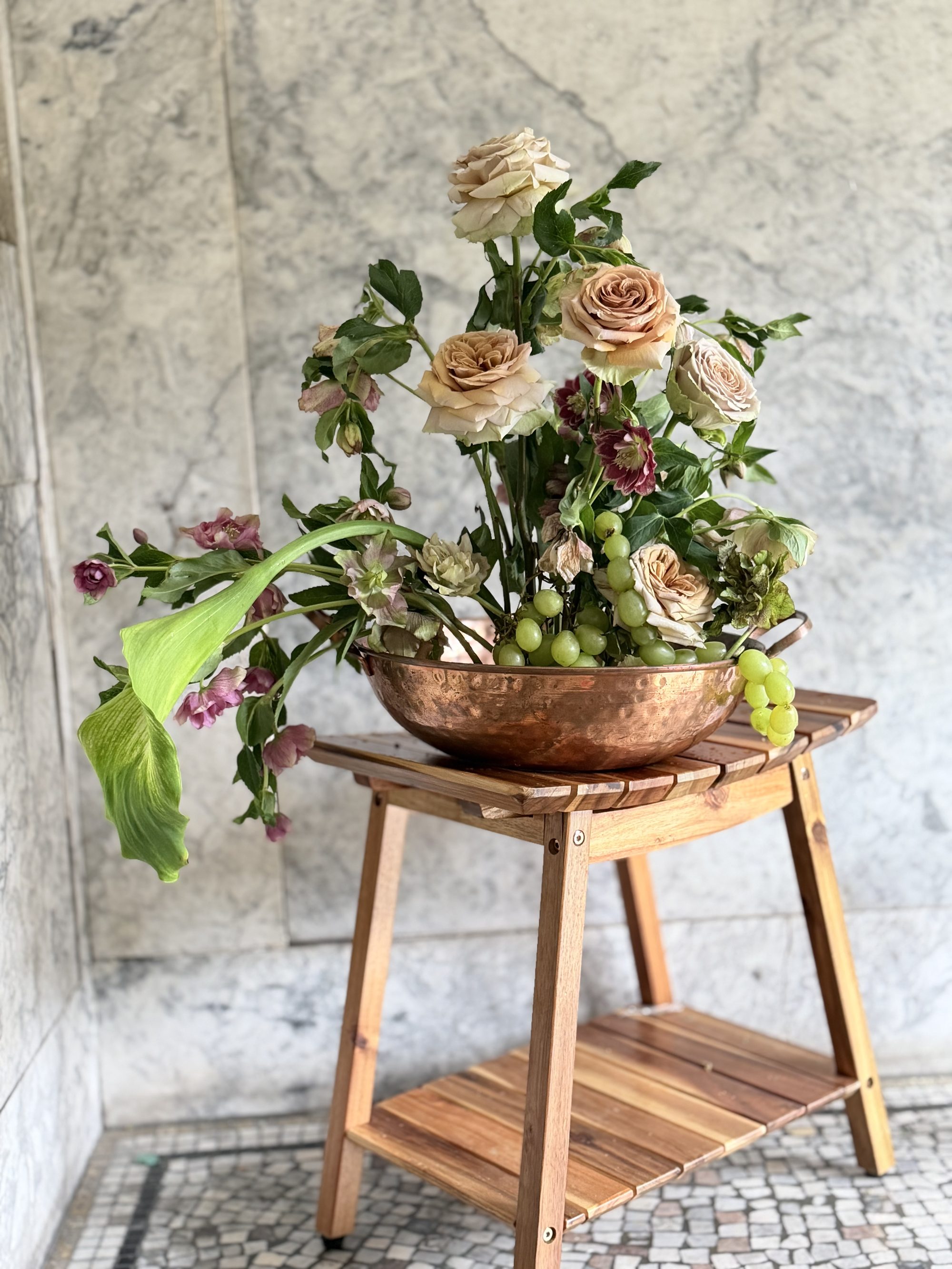 Deep red roses with cascading grapes in copper bowl on marble