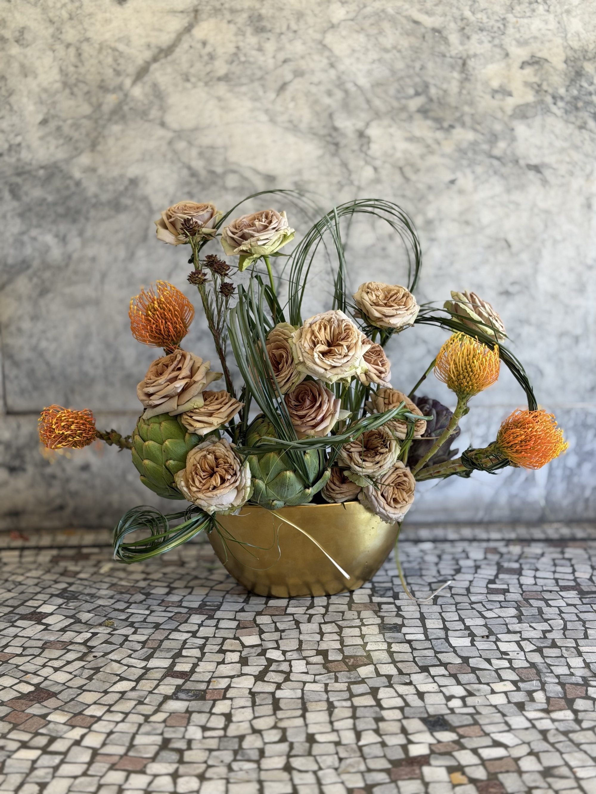 Toffee-colored roses with artichokes in low bowl against marble