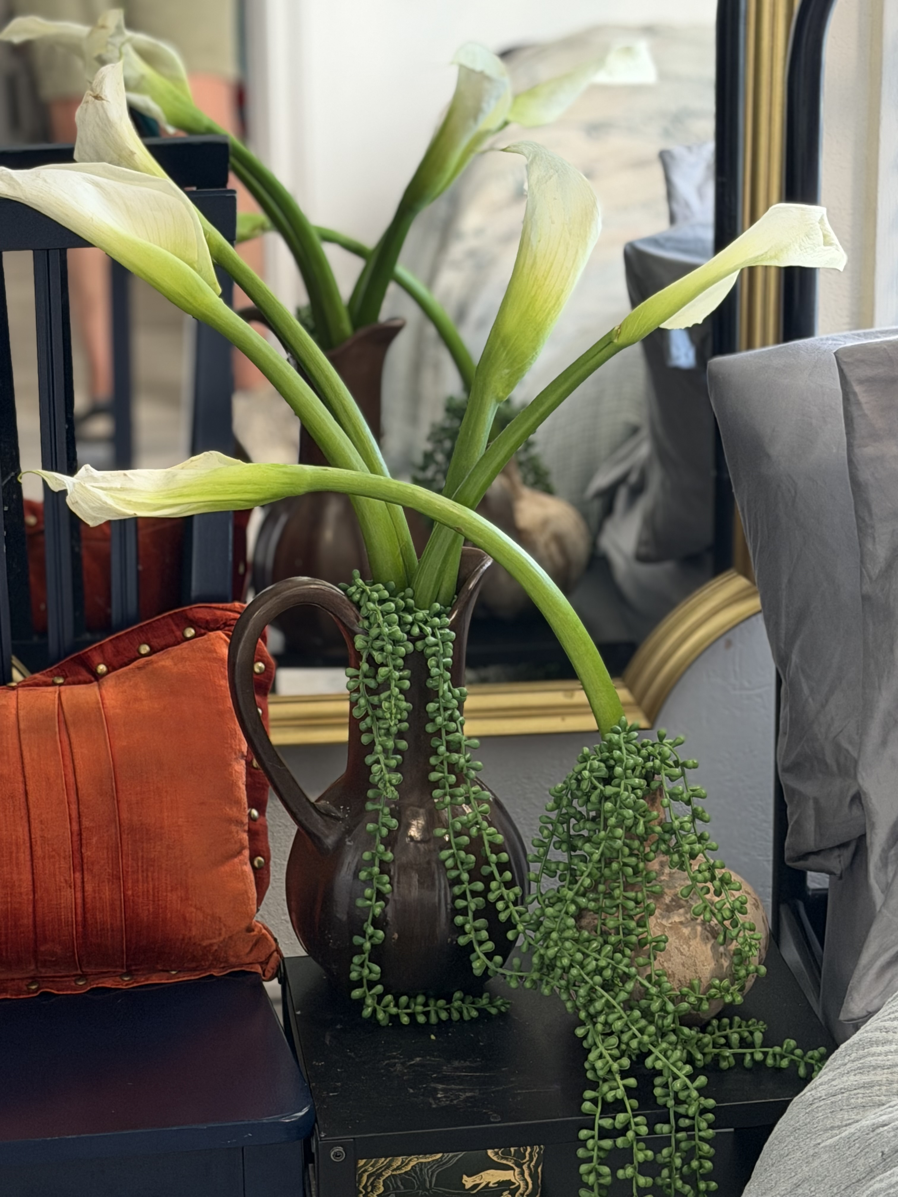 Calla lilies in a dark ceramic pitcher with trailing string of pearls