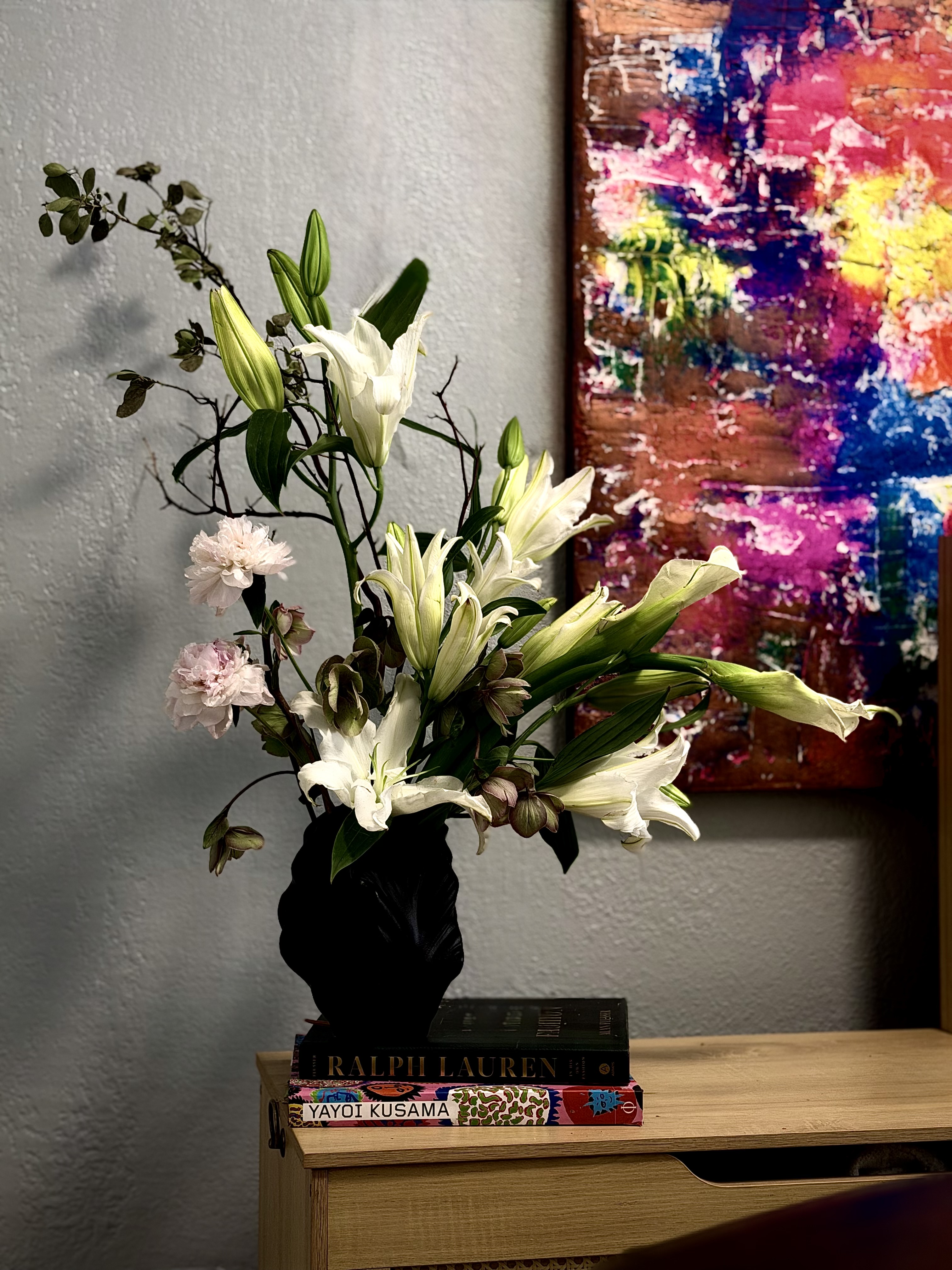 White lilies with dark branches in a sculptural black vase atop Ralph Lauren and Yayoi Kusama books