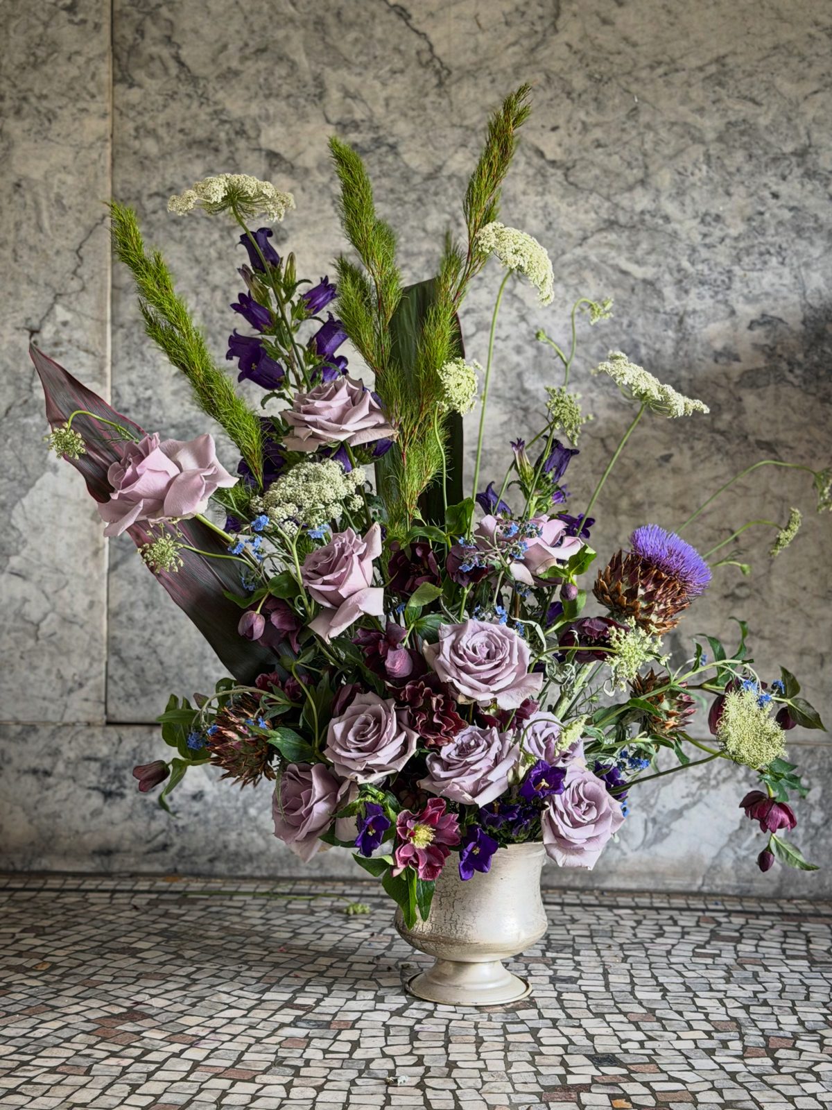 Example of The Full Moon — muted purple roses, artichoke, and Queen Anne's lace in a stone urn