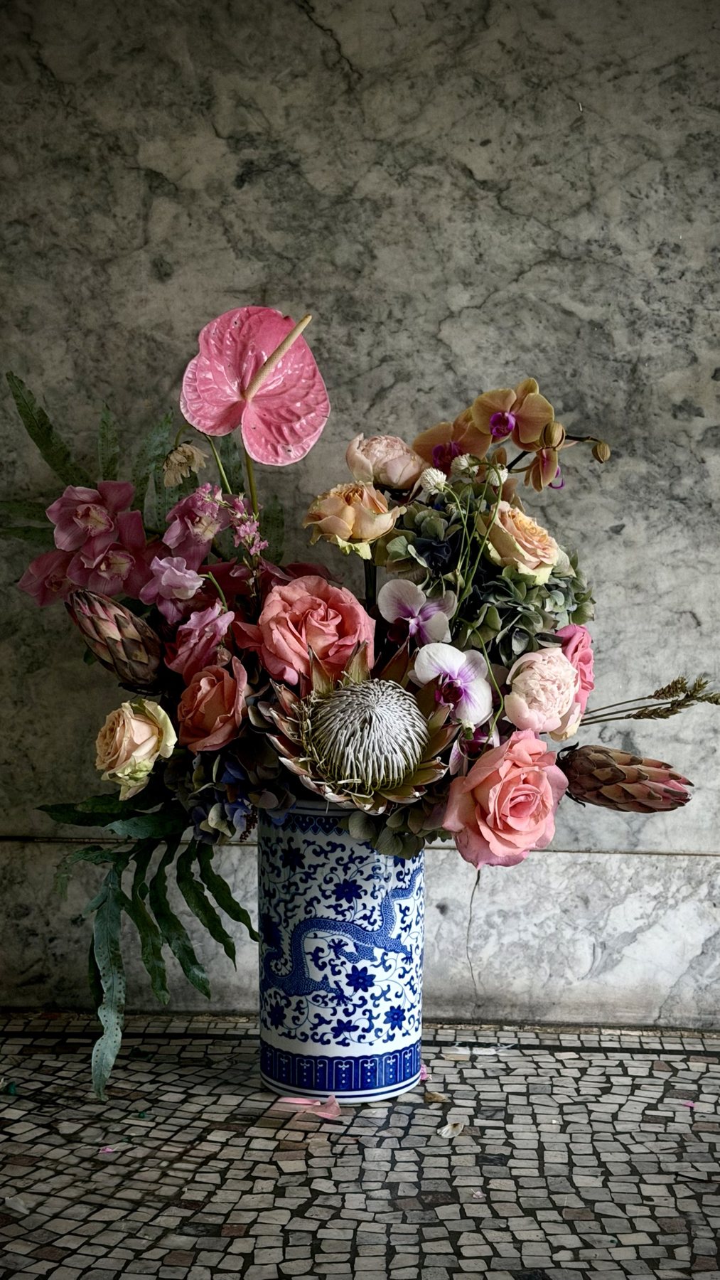 A sculptural dragon vessel carrying a dramatic floral composition with protea