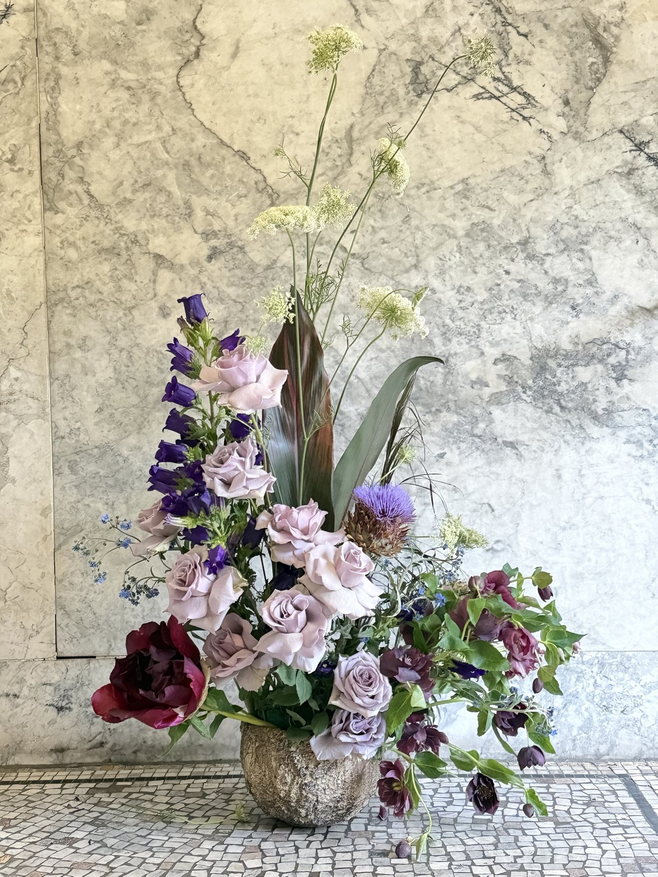 Garden roses, campanula and tulips in a stone pot, with Queen Anne's lace above and hellebores bowing downward