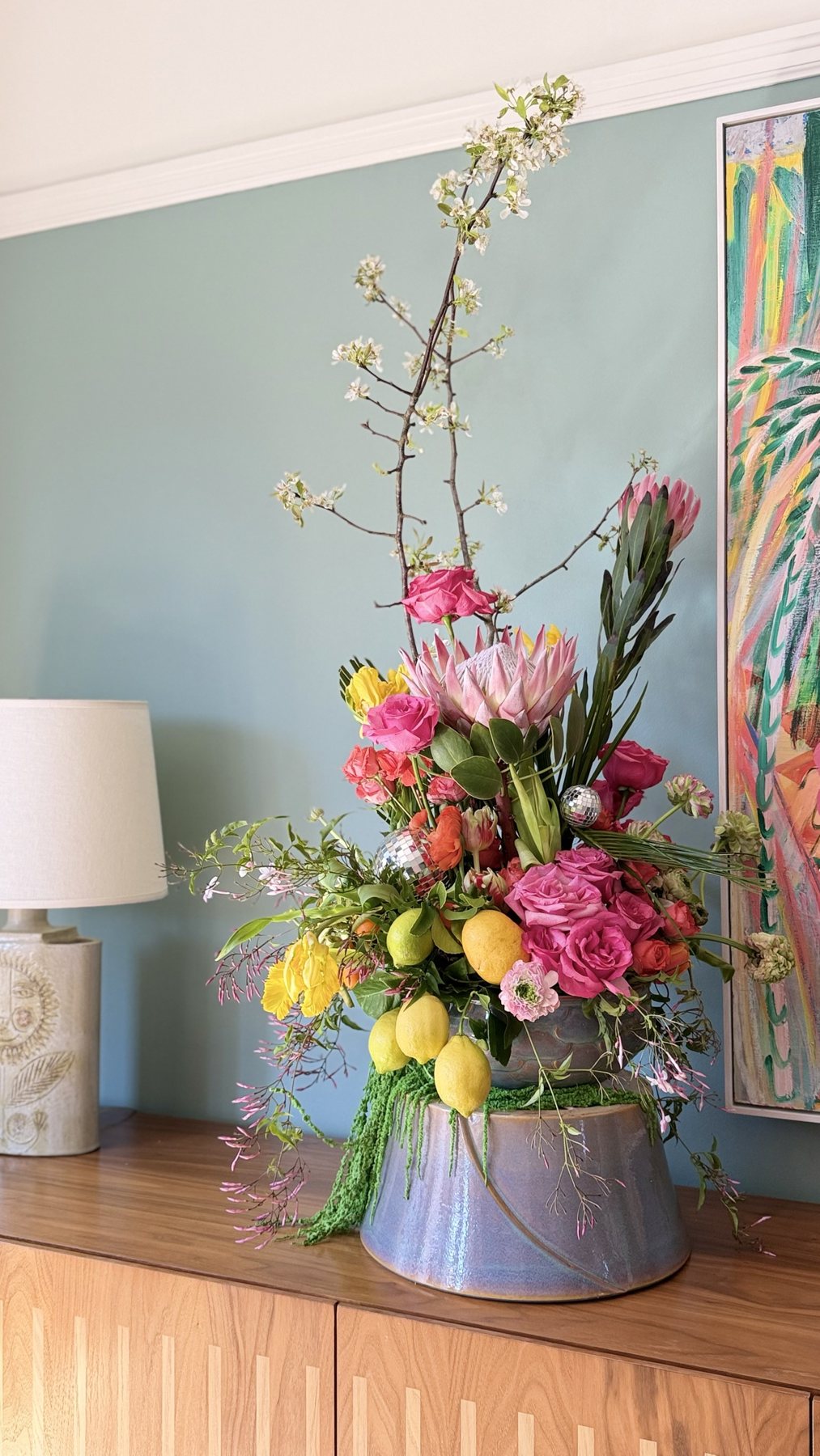 King protea, garden roses, parrot tulips and lemons spill from lilac ceramic beside disco balls